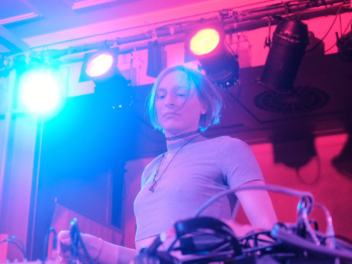 Live performance under pink and blue stage lights, hands on hardware synthesizers