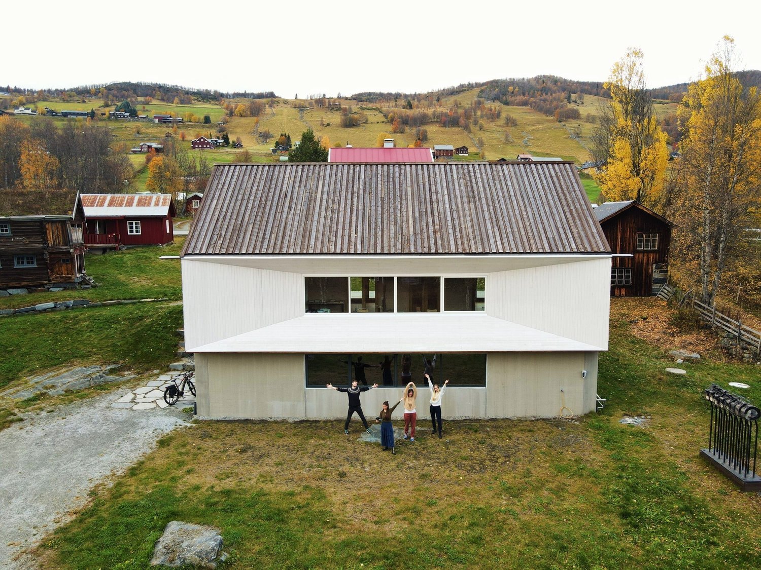 Aerial view of the barn building at Leveld Kunstnartun with four people in front of it, surrounded by autumn hills